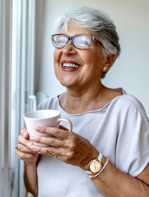 Senior resident cheerfully holding a cup of Mira Vie by the window.