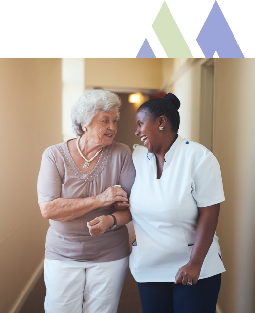 At Mira Vie at Green Knoll retirement home, a devoted caregiver gently assists an elderly resident while walking down the corridor.