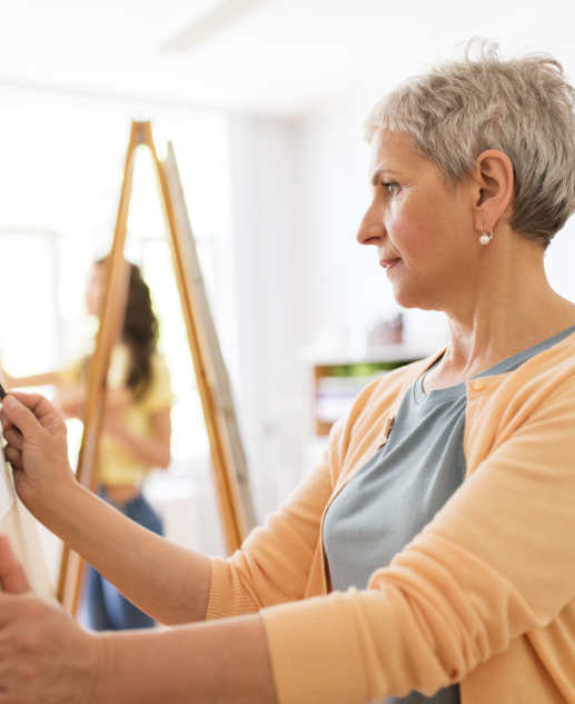 At Brookfield's Mira Vie Retirement Community, an experienced woman joyfully engages in canvas painting, with a youthful woman accompanying her in the serene backdrop.