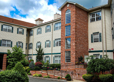 Our charming retirement community at Mira Vie, featuring residential apartments accented with brick and white siding. Comfortable senior living under cloud-kissed skies. Contact us for more details.
