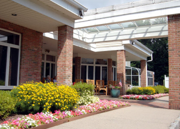 A welcoming atmosphere at our retirement community, featuring a beautifully maintained entrance with brick walls and a covered walkway. Colorful flowerbeds enriching the surroundings. For more information, get in touch with Mira Vie today!