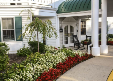 Visit our retirement community, graced with stunning red and white flowers and relaxing rocking chairs under a verdant canopy. For more details, please get in touch with Mira Vie - your gateway to comfortable senior living.