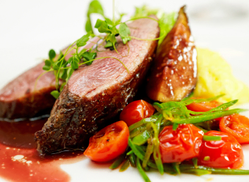 A beautifully plated pan-seared duck breast accompanied by cherry tomatoes and green vegetables, finished off with creamy mashed potatoes and a delightful red wine reduction at Mira Vie Retirement Community in Brick.