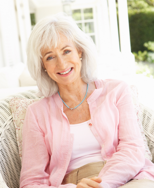 Joyful living at Mira Vie at Forsgate retirement community, where senior residents can relax outdoors, like a happy elderly woman in a pink shirt, comfortably seated in her wicker chair.