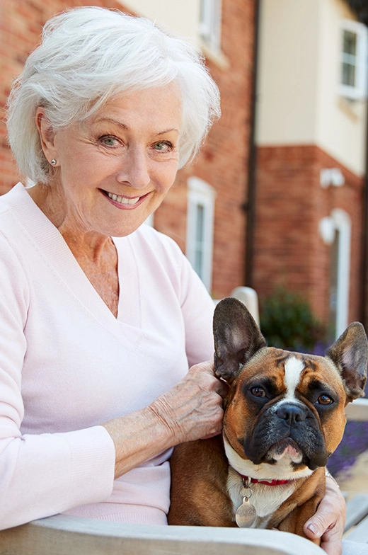 Delightful senior woman enjoying independent living with her French bulldog on a bright, sun-filled day at our retirement community.