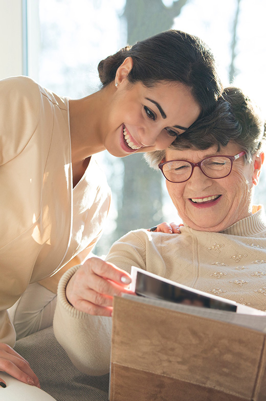 Young and elderly women joyfully sharing memories in our senior living community’s memory care facility.