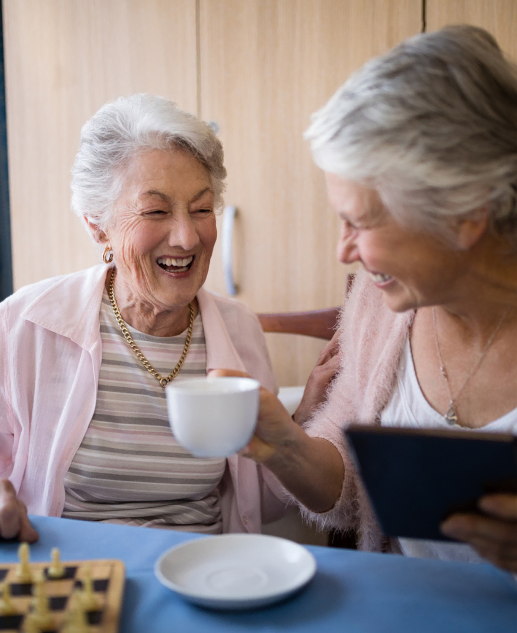 Elderly women sharing joy over tea and chess at Montville's Mira Vie retirement community.