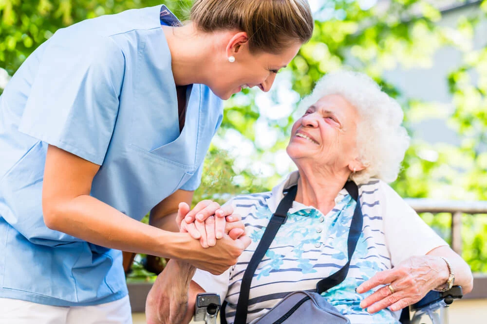 The heart of our retirement community as compassionate healthcare professionals assist our happy residents, like this cheerful elderly lady enjoying her time outdoors in a wheelchair. The true value of assisted living.