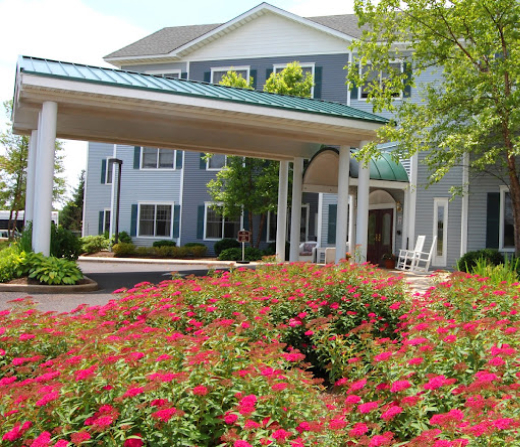 Mira Vie retirement community offers a picturesque two-story blue and white edifice with a sheltered entryway. The tranquility of our lush garden blossoming with vibrant red flowers right at your front door.