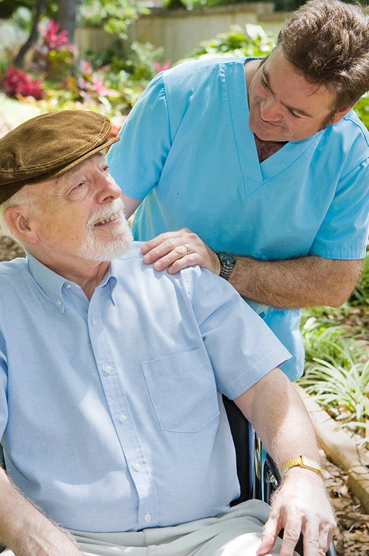 Respite care from our dedicated caregiver, seen in blue scrubs, assisting a senior resident with mobility aid in our outdoor premises. Ideal for SEO: Caregiver Assistance at Senior Living Community.