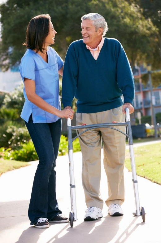 Experienced healthcare professional offering premium senior living services, assisting an elderly man with a walker in an outdoor setting.
