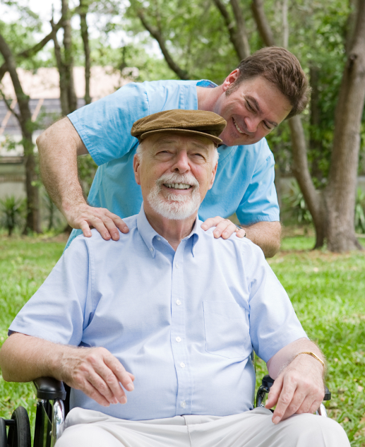 Elderly gentleman in wheelchair, accompanied by a younger man, delighting in the outdoor setting of Mira Vie at Tinton Falls assisted living community.