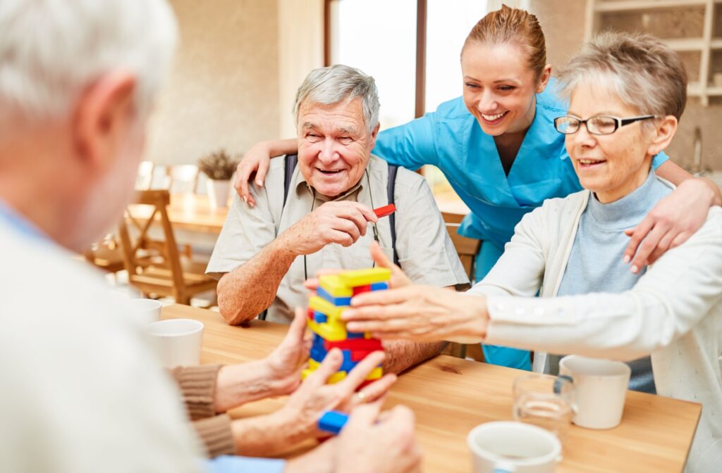 Group of older adults engaged in a fun building activity at a table, supported by a smiling caregiver.