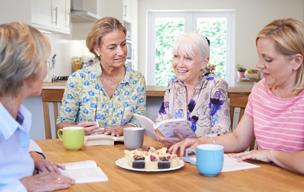 A group of seniors sit around a table and discuss the book they read for their book club over snacks and tea.