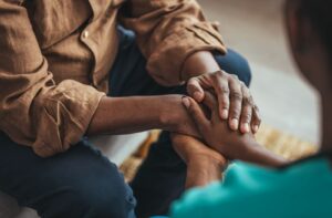 Close-up of a young woman holding a senior man's hands in a comforting, empathetic gesture.