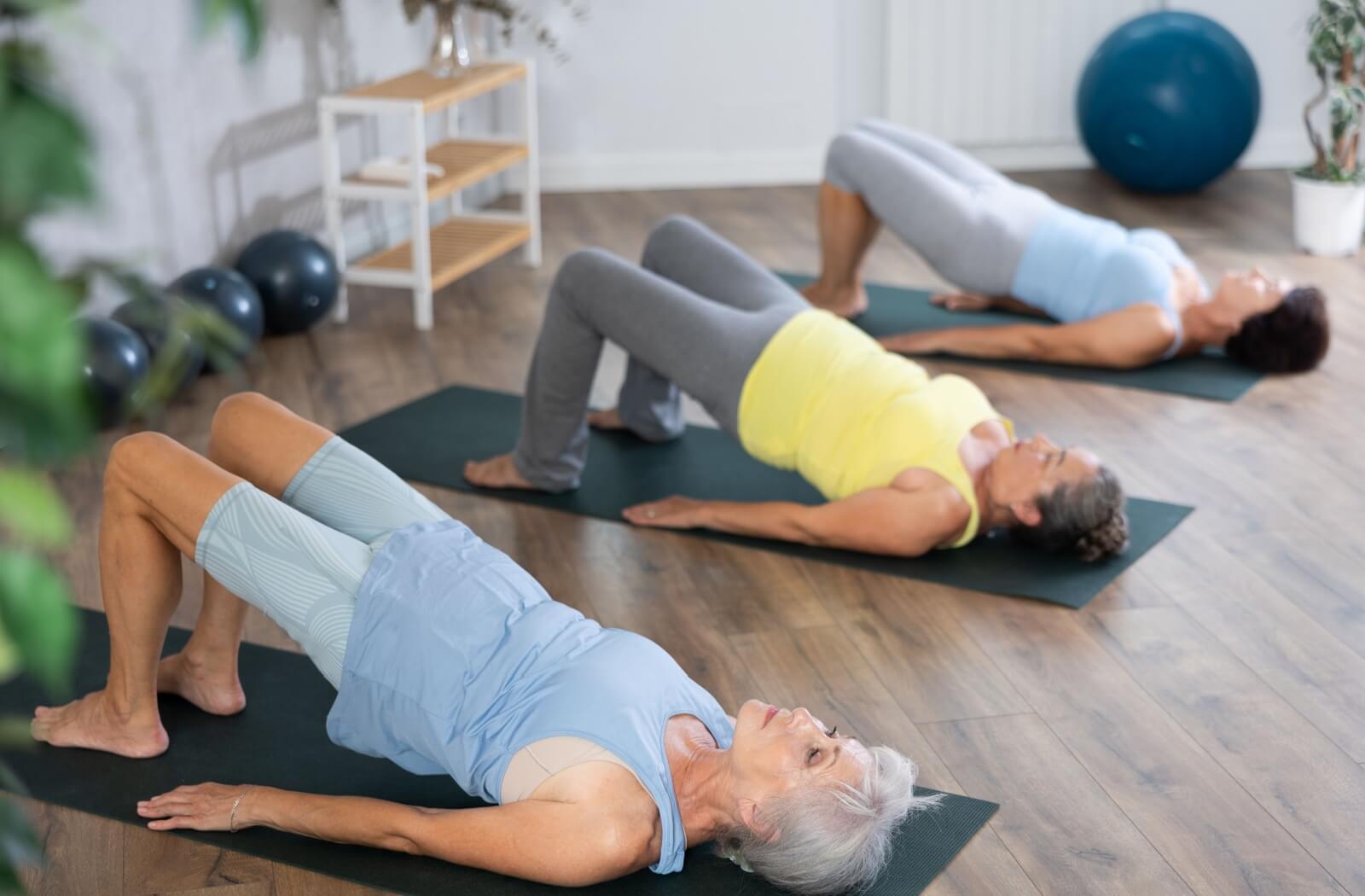 Older adults in a group exercise session performing bridge poses on mats in a bright fitness room.