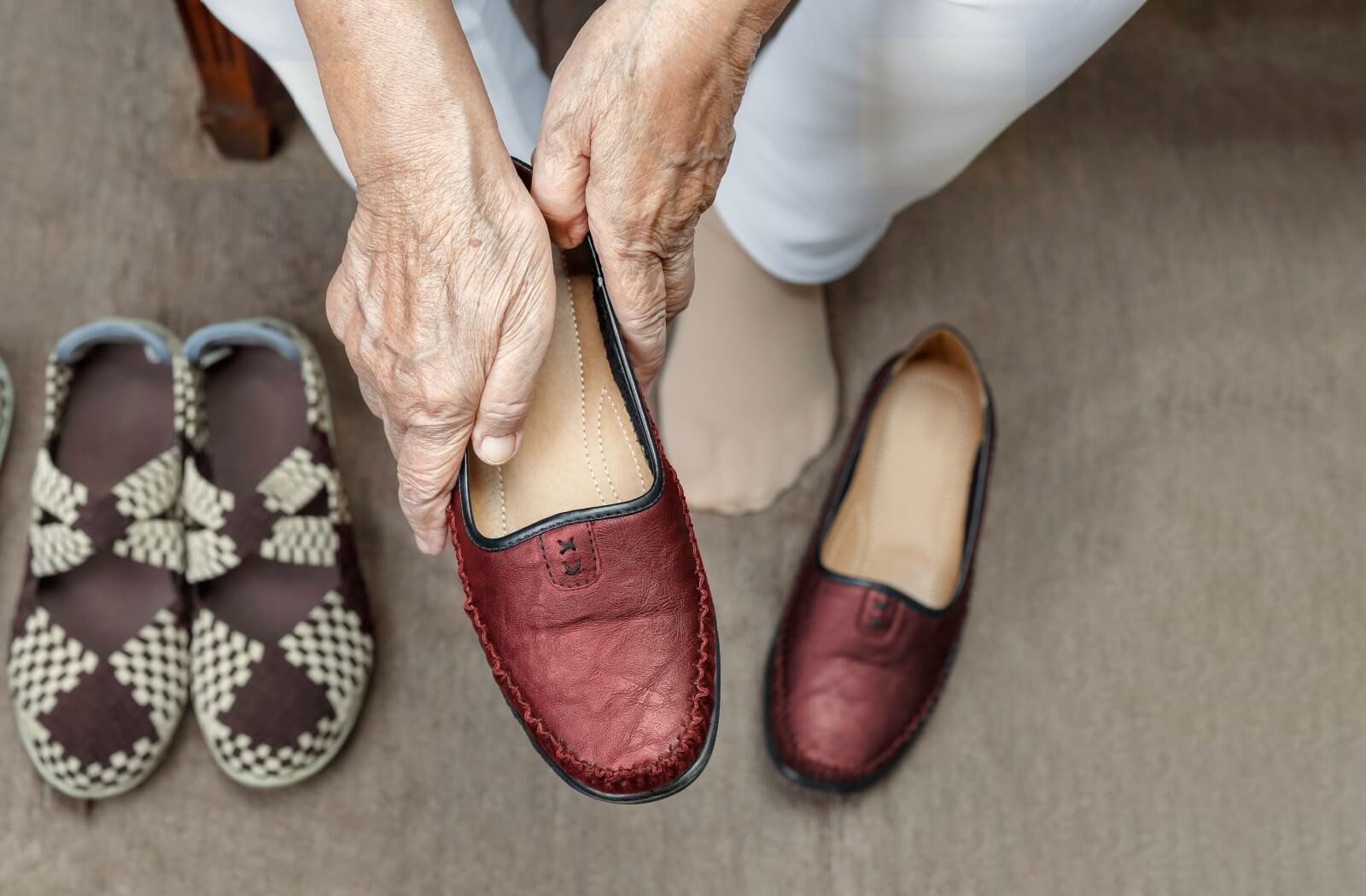 A senior holds one of a pair of red slip-on shoes to try on while out shopping for dementia-friendly footwear