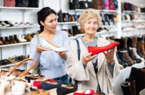 An adult helps their older parent shop for slip-on shoes to help reduce their fall risk