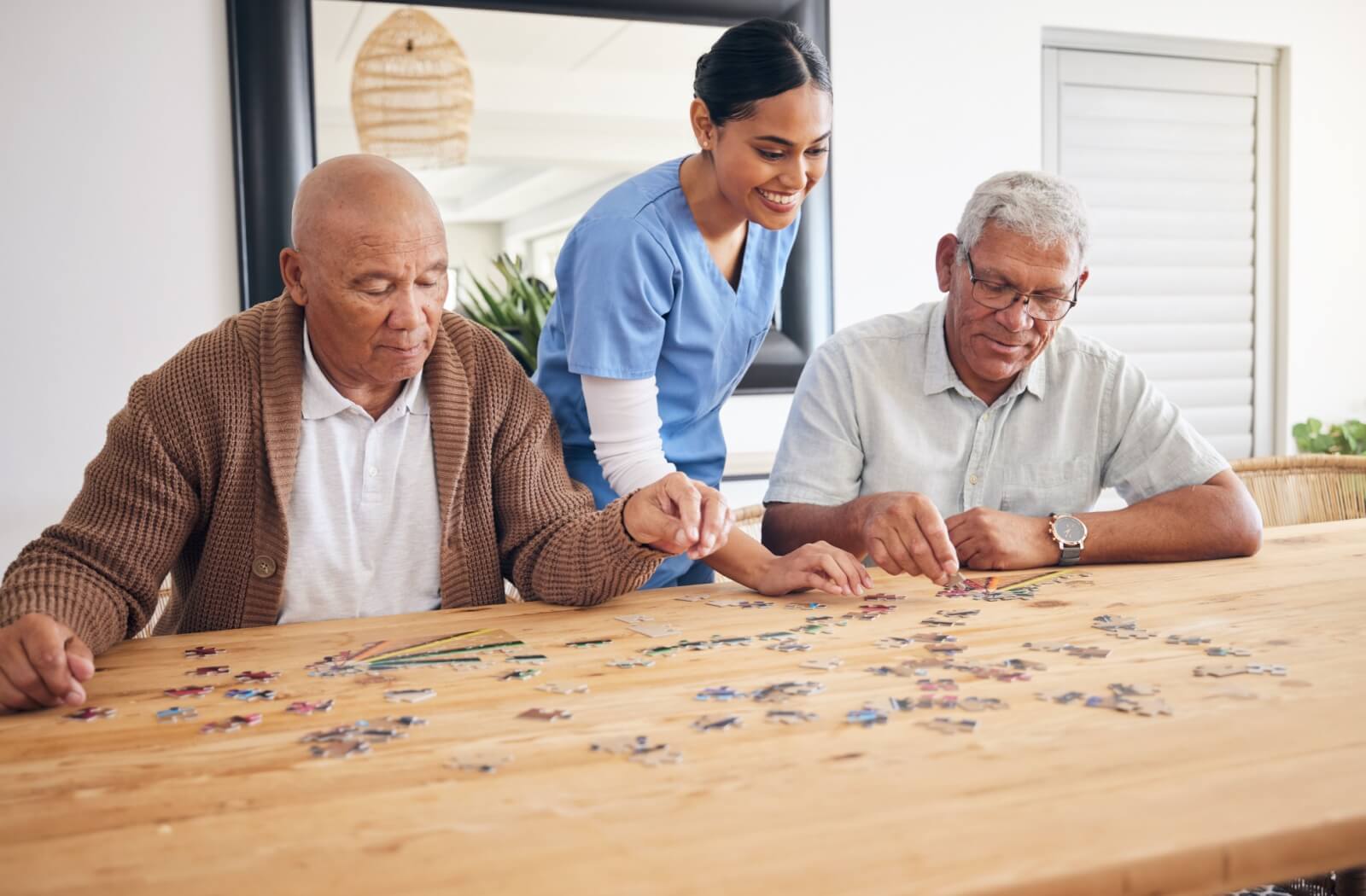 Two older adults working on a puzzle with the help of a caretaker.