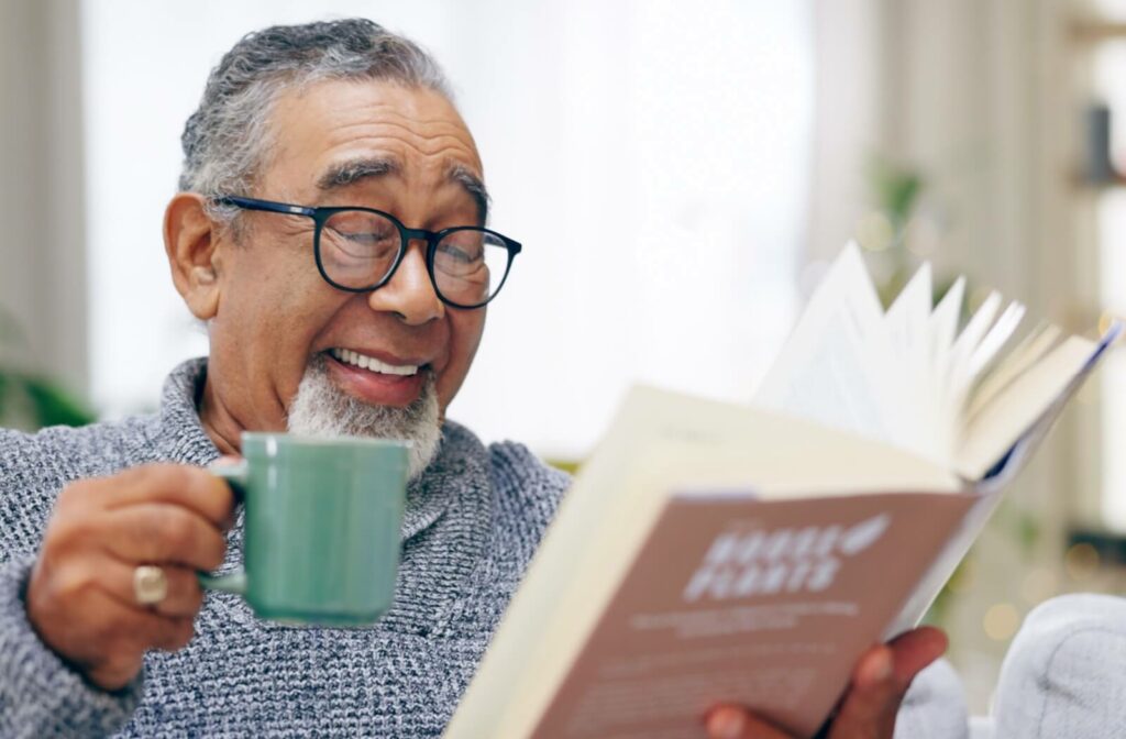 A seniors holding a coffee mug laughs at a joke in the book they’re reading over breakfast