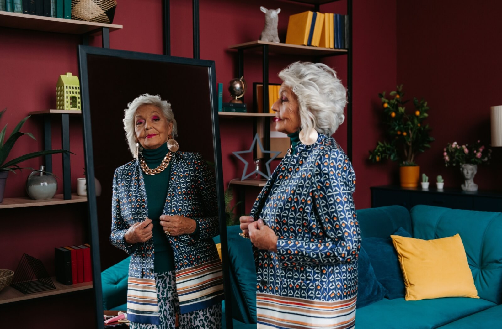 stylish senior looks at themselves in the mirror as they hold onto the edges of their silk blazer