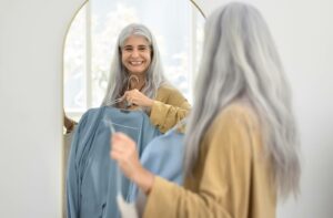 A smiling senior holds up a blue jumpsuit in the mirror as they prepare to get dressed in the morning