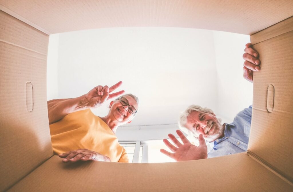 Happy elderly couple looking down into a cardboard box, sorting items for downsizing.