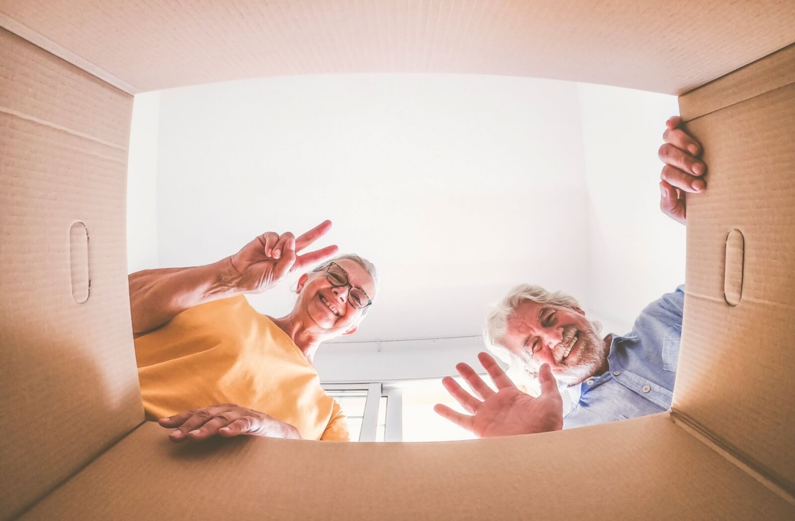 Happy elderly couple looking down into a cardboard box, sorting items for downsizing.