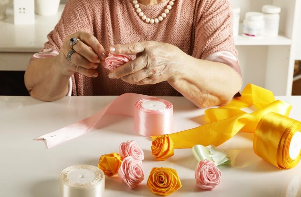 A senior in a pink shirt folds origami roses out of pink, yellow, and white velvet ribbon