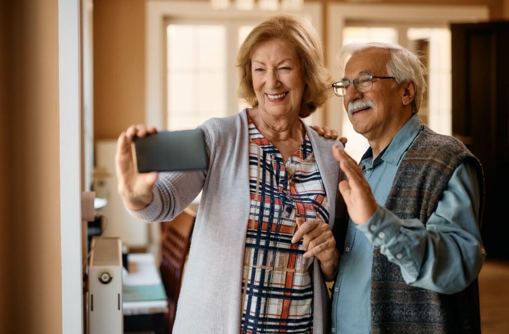 A senior couple video calls loved ones on their phone to talk about how their new assisted living home is treating them