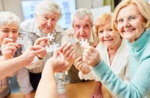 A group of seniors hold up white puzzle pieces to showcase the memory training activity they’re doing together
