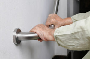 An older adult gripping a sturdy handrail, highlighting the importance of accessibility and fall prevention in assisted living communities.