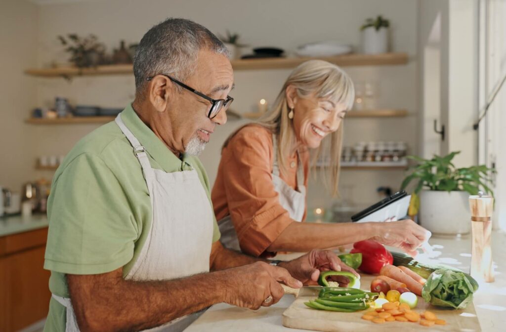 An older couple laughs as they cook a delicious meal together.
