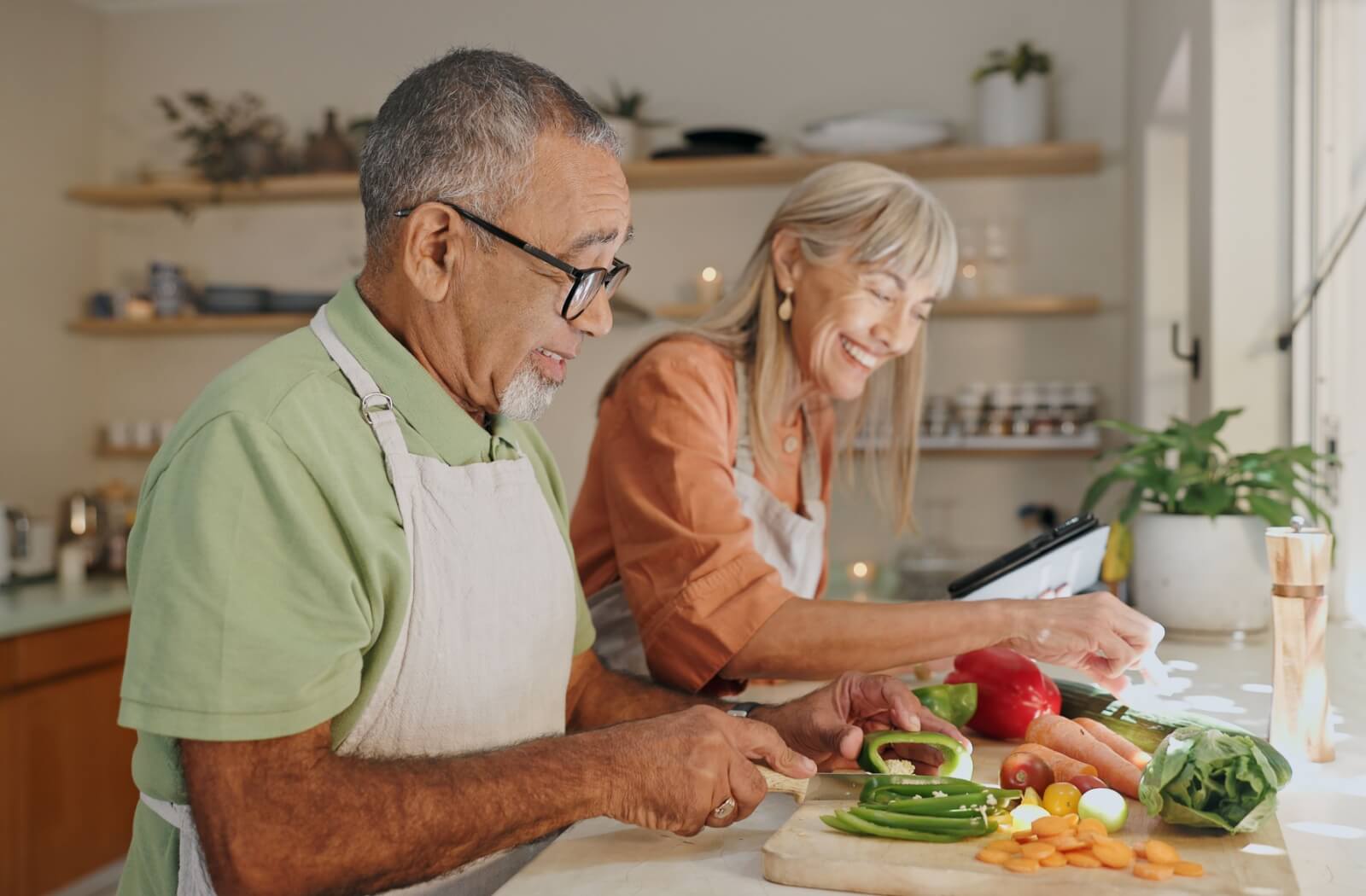 An older couple laughs as they cook a delicious meal together.