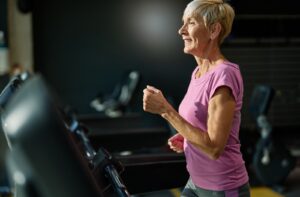 A smiling seniors takes advantage of their community fitness center and walks on a treadmill.