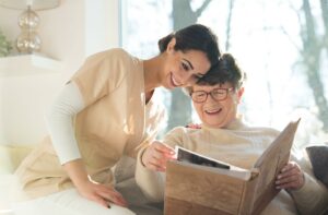 A nurse laughs along with a senior as they flip through a photo album, reflecting and reminiscing