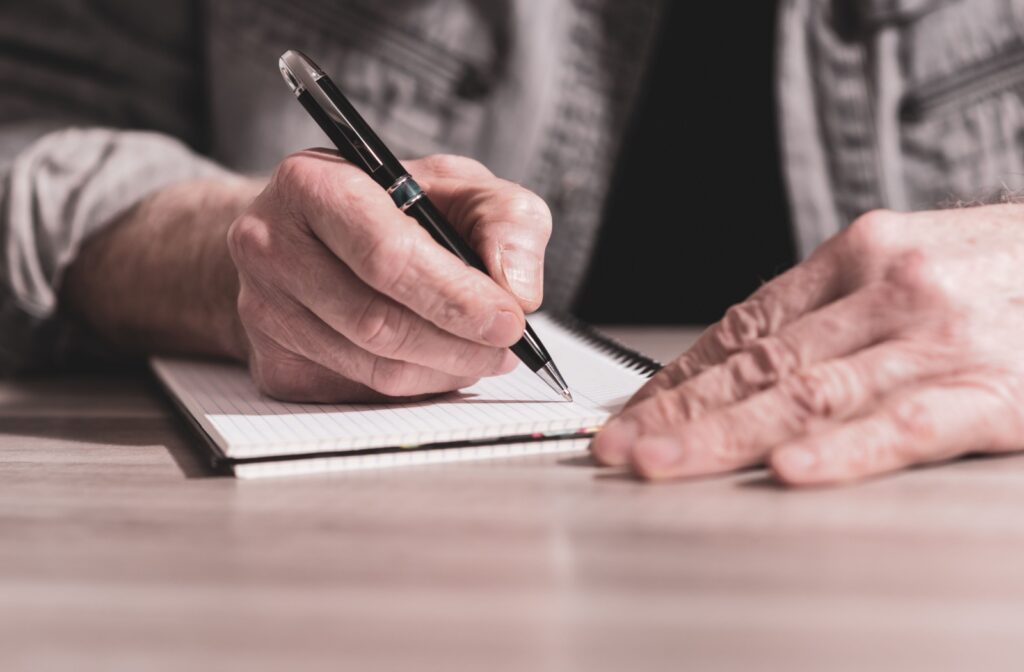 lose-up of an older adult's hands holding a pen and preparing to write in their notebook
