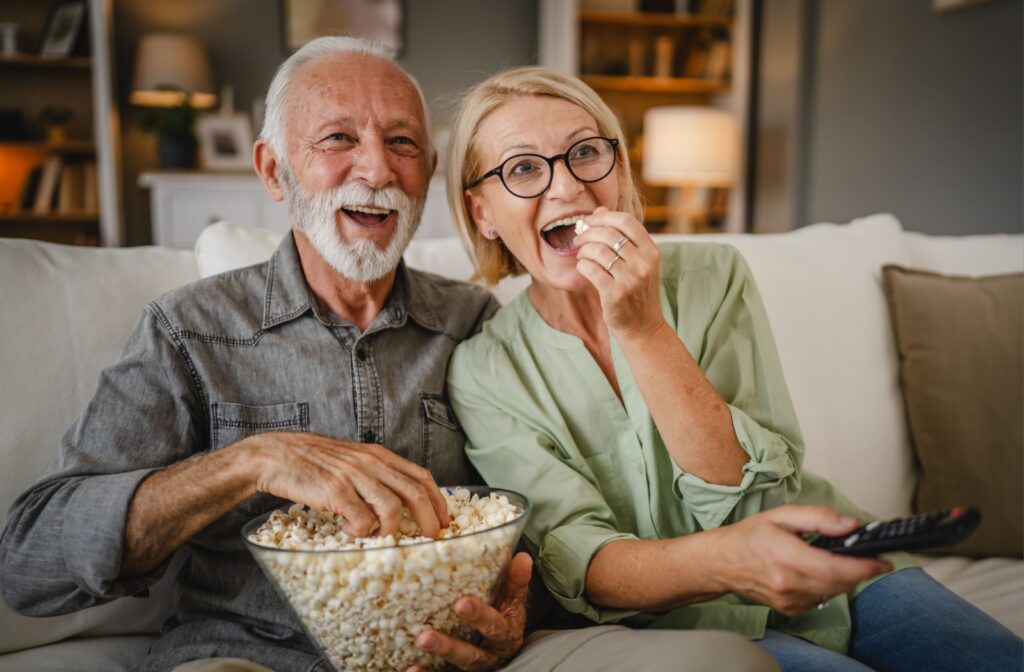 A happy senior couple enjoys a film together and shares a big bowl of popcorn.