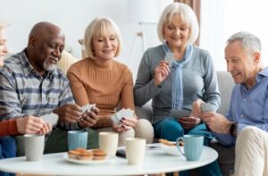 A group of friends in assisted living gather together to play cards while enjoying coffee and snacks.