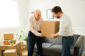 An adult helps their senior parent lift moving boxes.