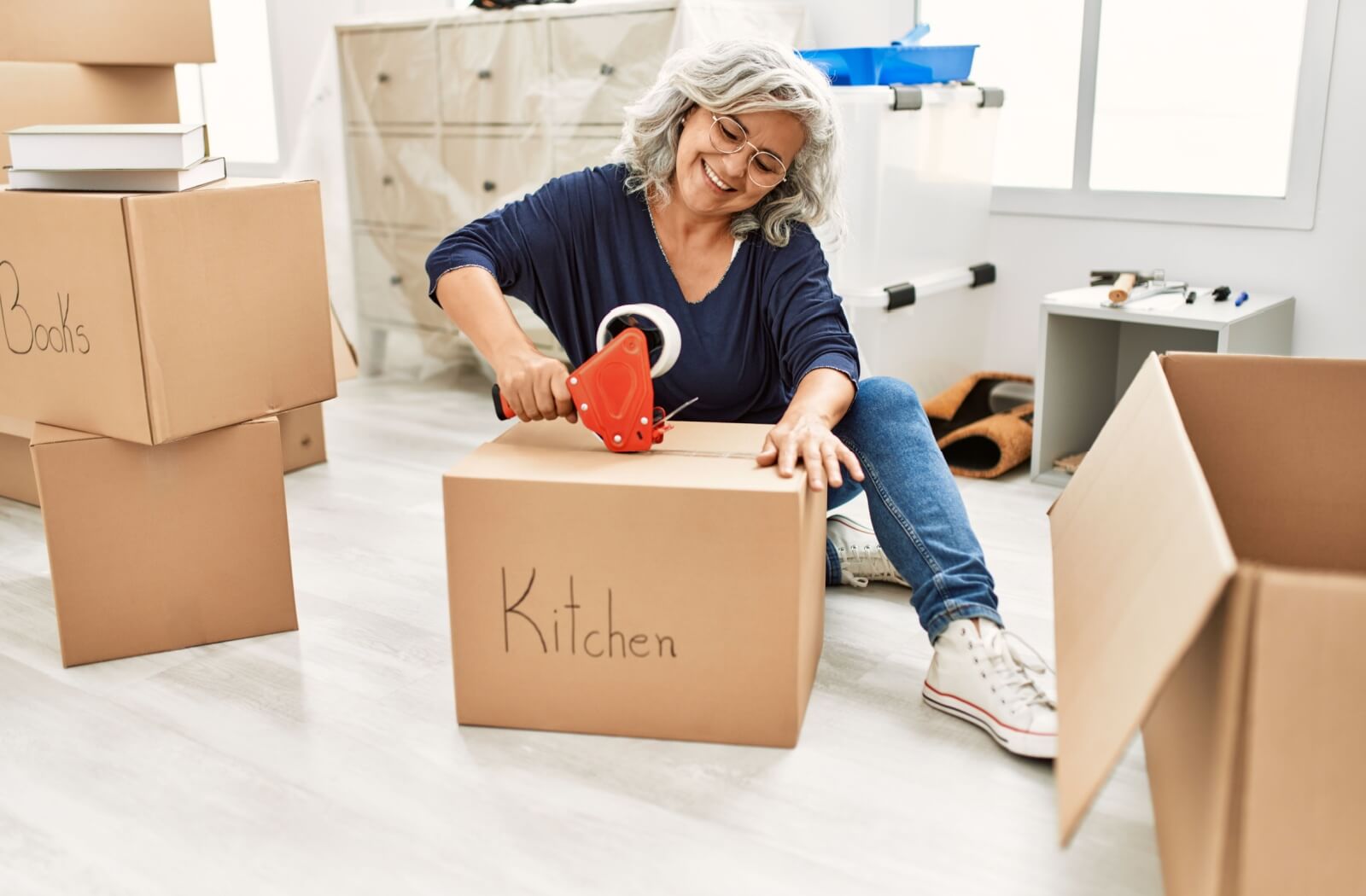 Senior person packing up their personal belongings in boxes, taping closed the boxes labeled "kitchen"