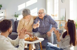 A mature couple in assisted living enjoys a family game night with their two adult children.