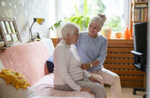 An adult child sits with their senior parent in their memory care condo.