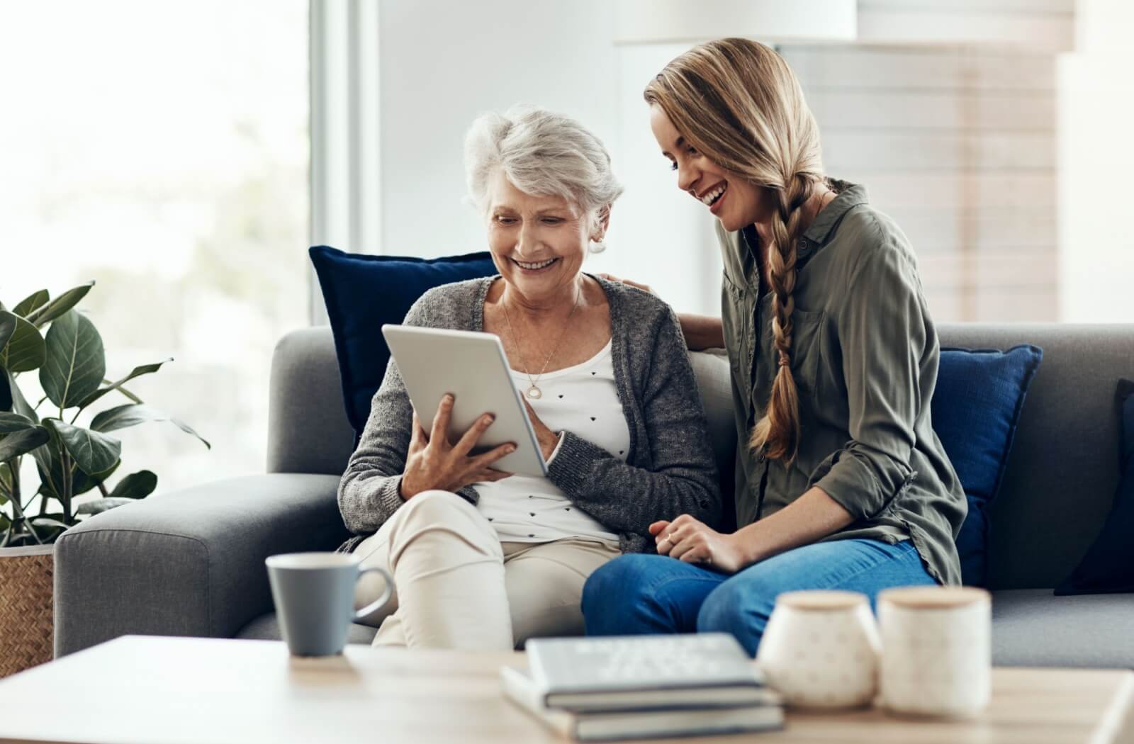 An adult child visiting their parent in assisted living while connecting with digital devices.