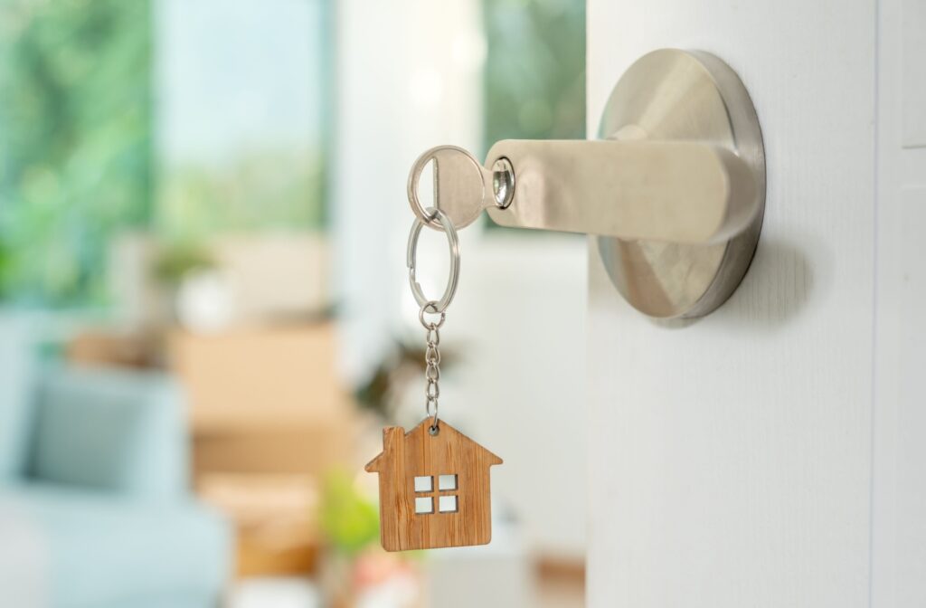 A key inserted in a door handle lock with a house pendant hanging from the chain.