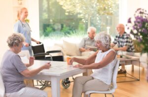 4 seniors and a nurse go about their days in a sunny common room at the community.