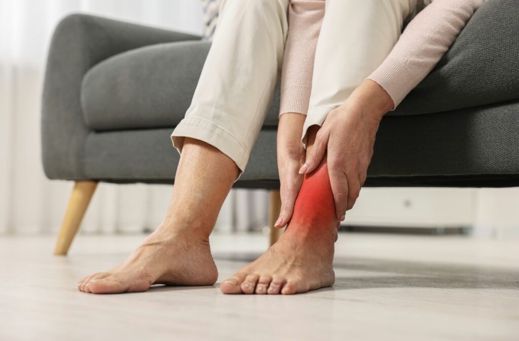 A senior sitting on a couch touches their painful, swollen ankle.