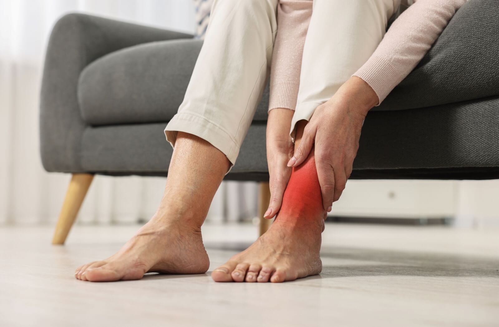 A senior sitting on a couch touches their painful, swollen ankle.