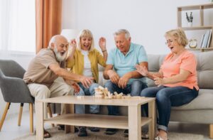 Four seniors play a game of jenga at a table in an assisted living community