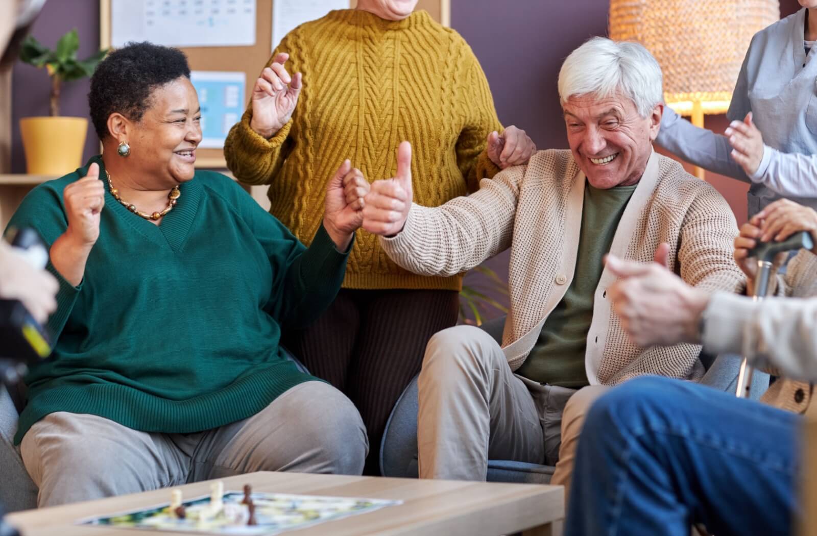 A group of happy seniors has a blast playing a board game together in their assisted living community's communal area.